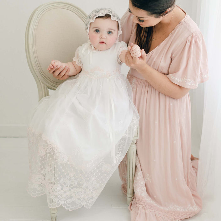Woman in a pink dress holding a baby in a white and pink lace dress and bonnet.