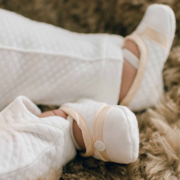 Boy wearing a pair of the Liam Booties made from soft quilted cotton with a champagne silk trim and accented with cotton ribbon and buttons on the toe. A soft elastic strap helps keep them on his feet