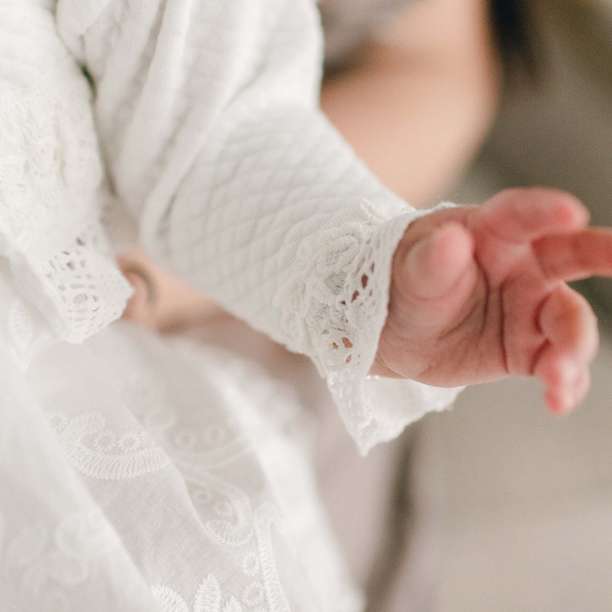 Baby's sleeve of the Lily Quilted Cotton Sweater showing the detail of the ivory cotton lace with rose and vine floral embroidery