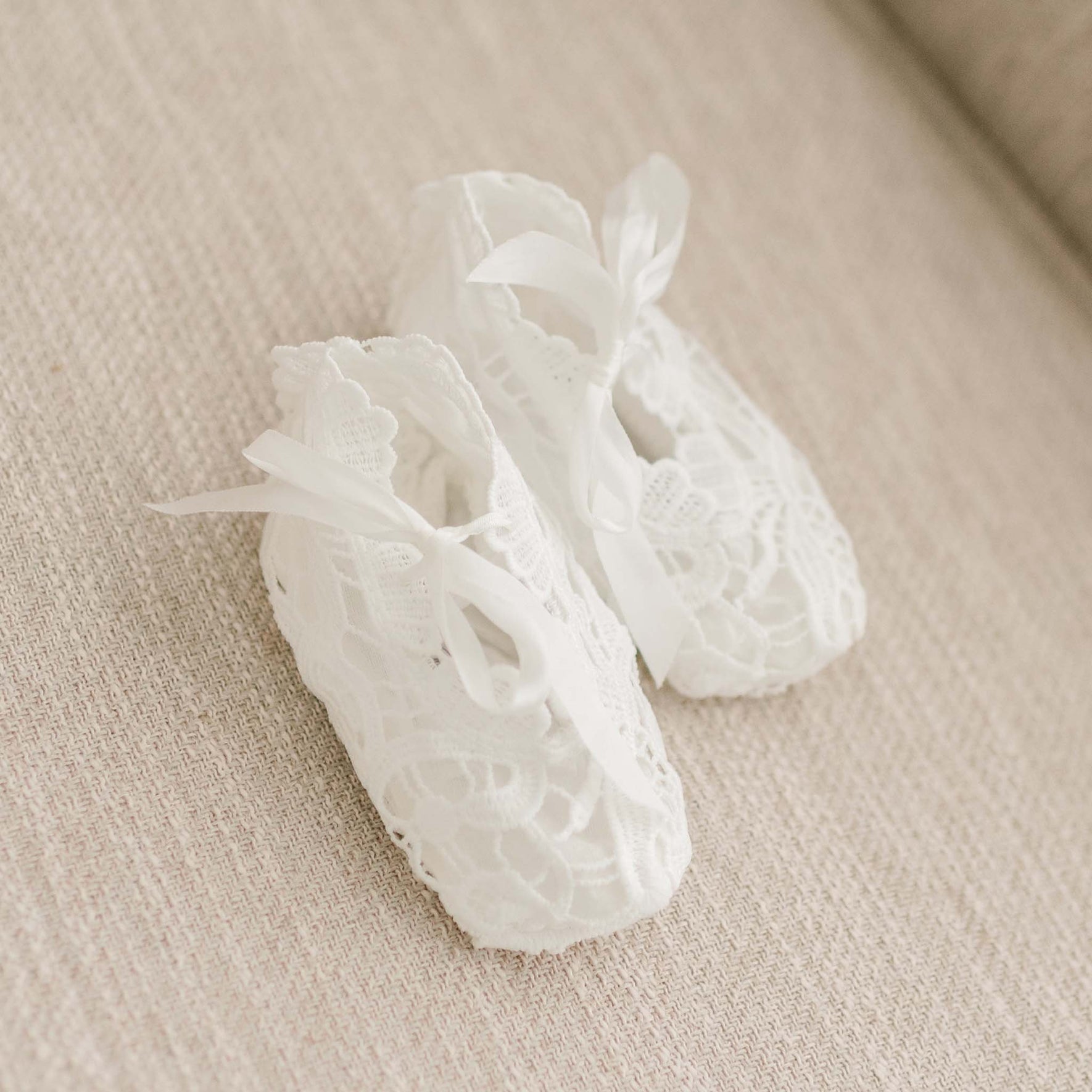Flat lay of the Lola Christening Booties, featuring light ivory lace and finished with silk bow ties.