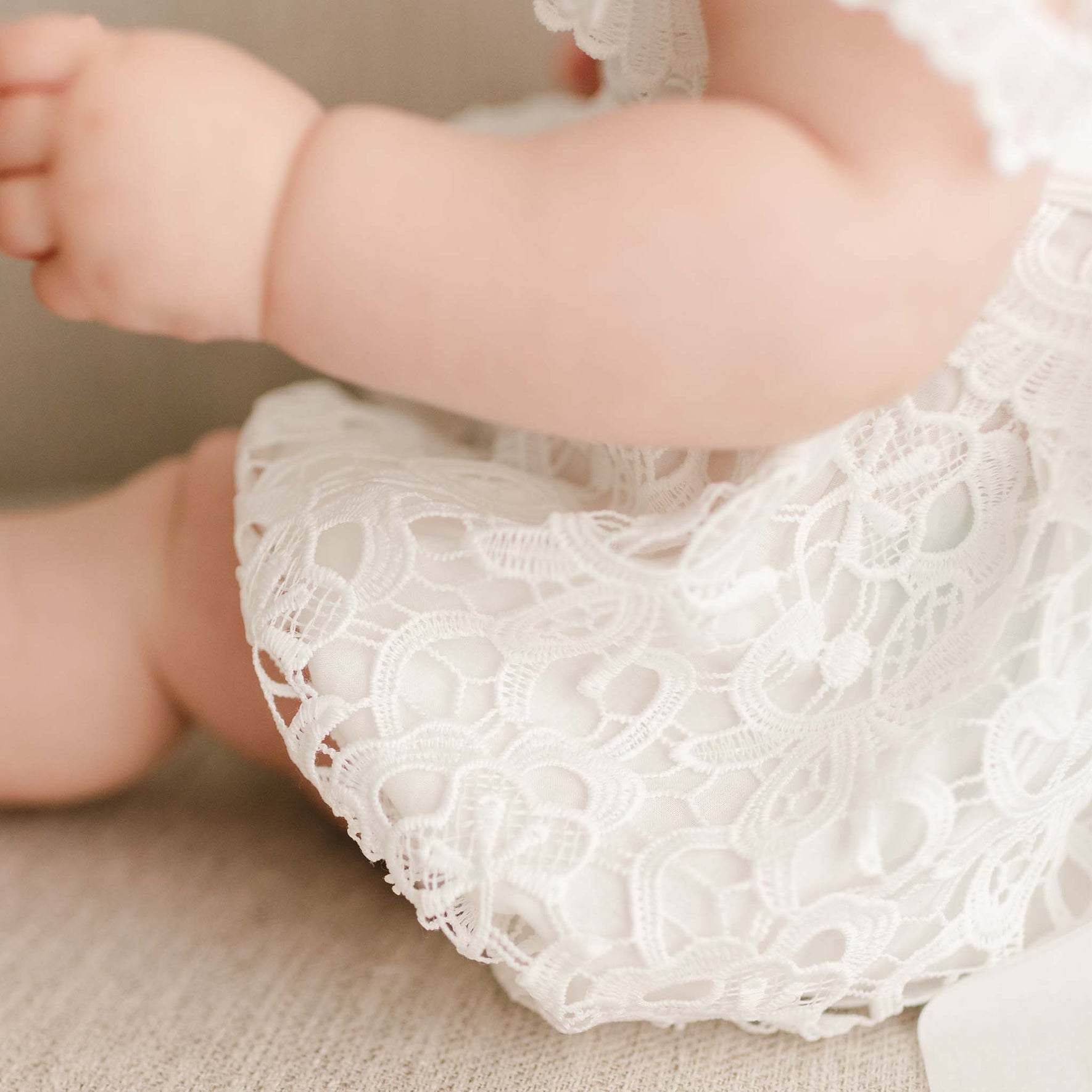 Detail of the Lola Lace Christening Romper worn by a baby girl, featuring intricate light ivory floral lace and a soft cotton lining.