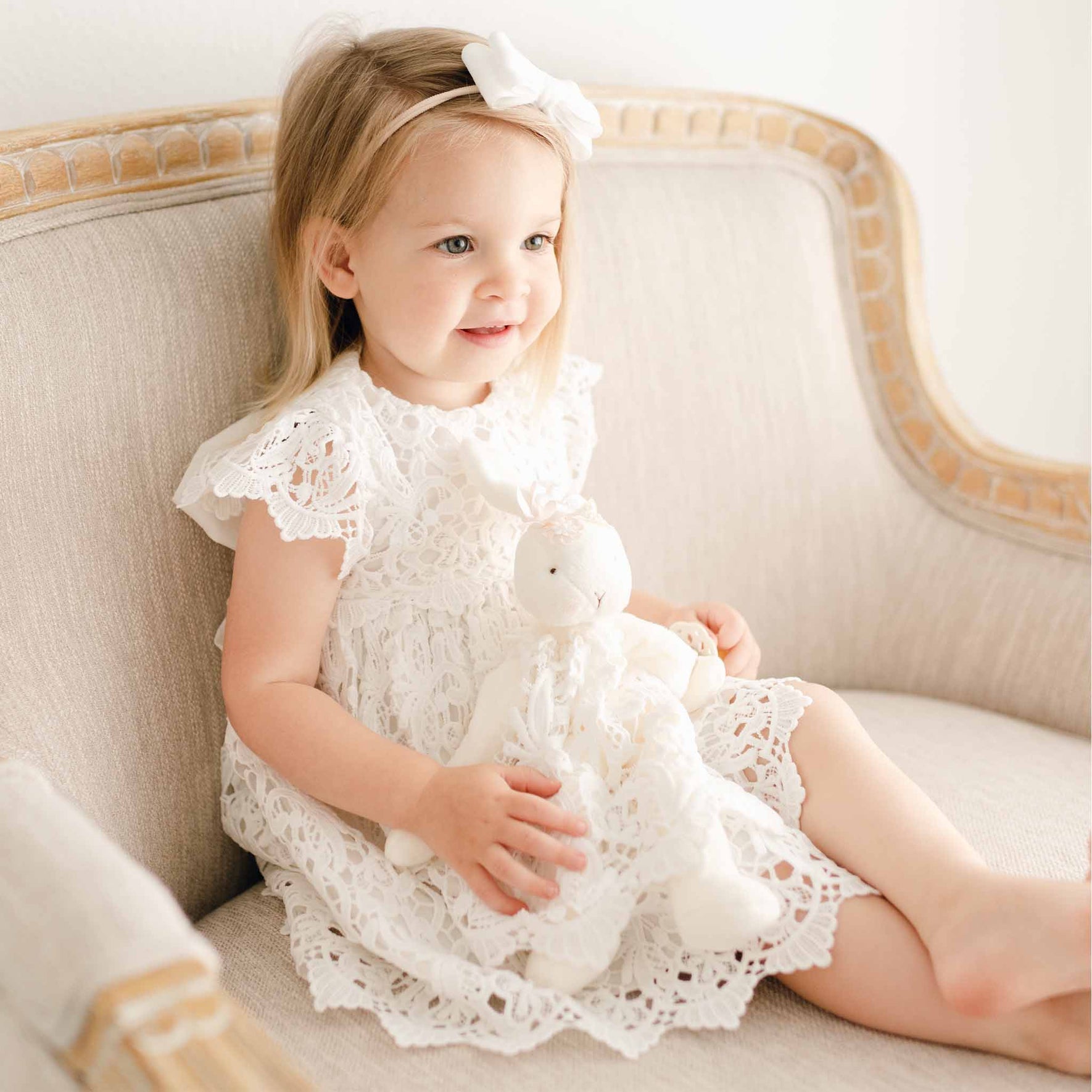 Baby girl wearing the Lola Dress. She is holding a Lola Silly Bunny Buddy pacifier holder with the same Lola Dress.