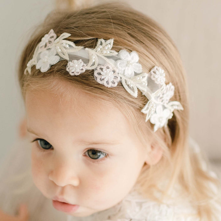 A close-up of the Lola Beaded Flower Headband on a toddler girl, showcasing the velvet band and detailed pastel pink and ivory flowers.