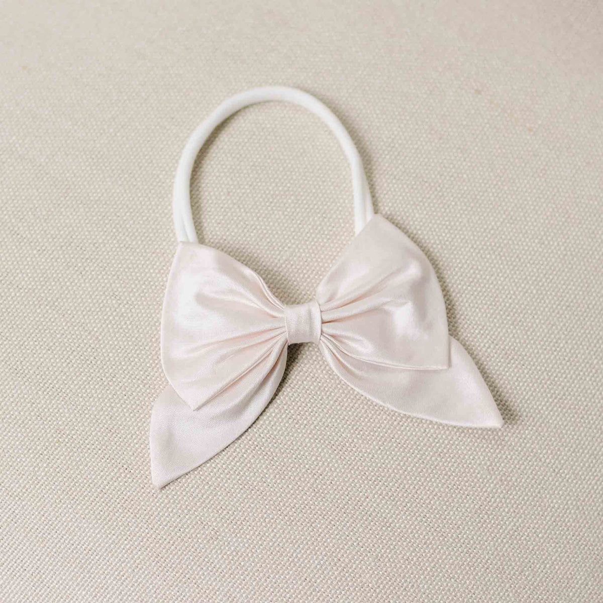 Flat lay of the Melissa Bow Headband on a beige background. Details show a large pink silk ribbon bow. Perfect for unique baby gifts. 