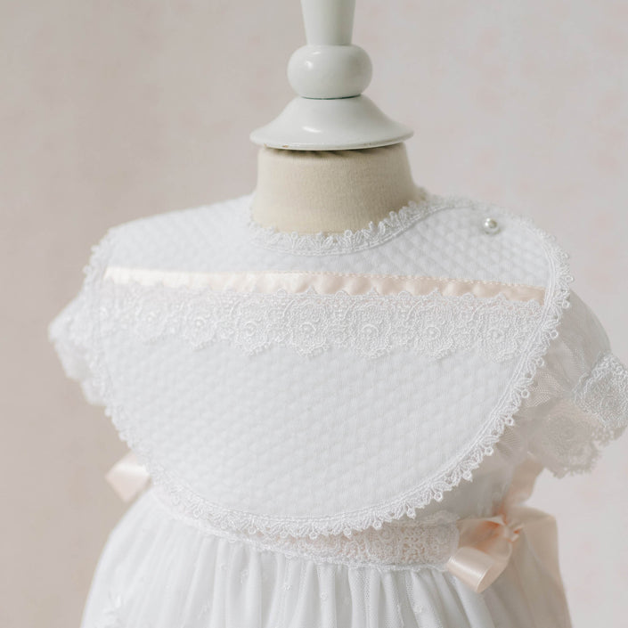 Close up photo of the Melissa Bib on a mannequin against a plain background. Details show white quilted textured cotton with Venice lace and silk ribbon. Perfect baptism gift from godparents.