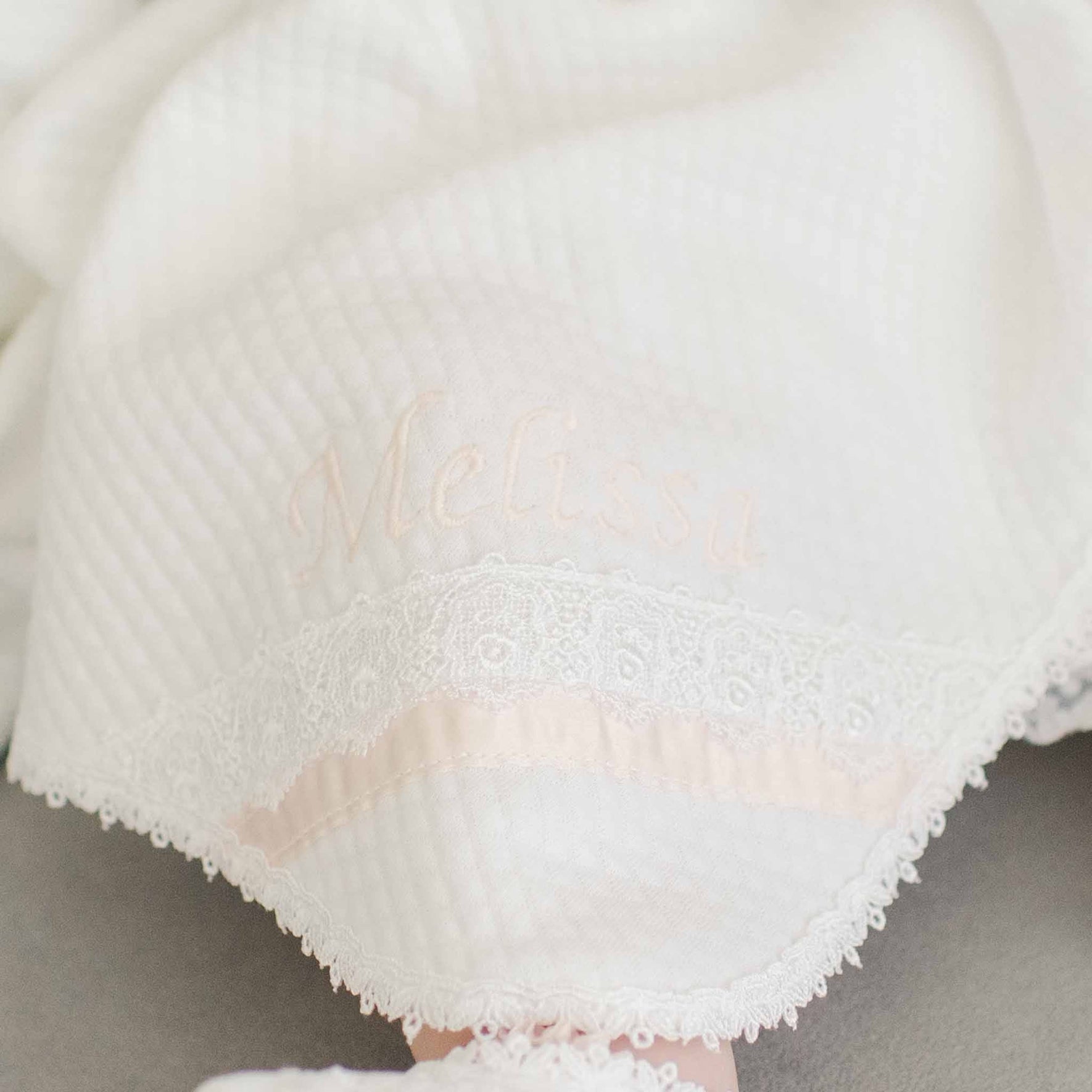 A Melissa Personalized Blanket with the name "Melissa" embroidered in light pink thread, crafted from quilted textured cotton. The blanket features a Venice lace trim with an additional pink ribbon detail running parallel to the lace edge, all handmade in the USA.