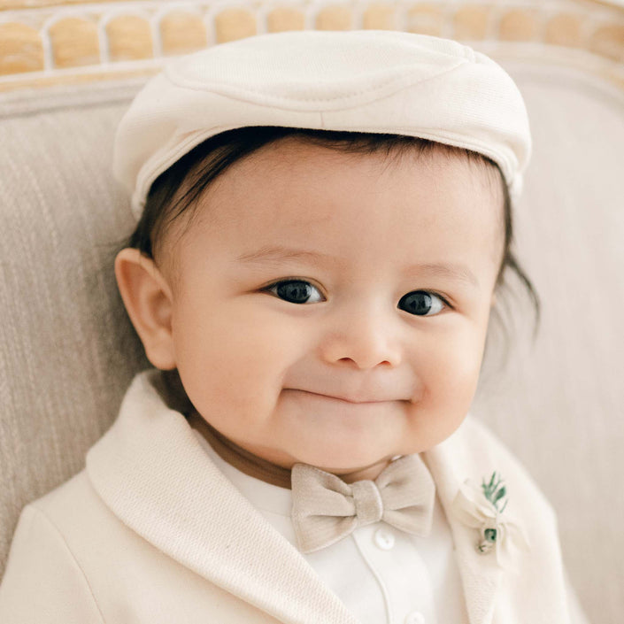 A baby smiling while wearing the Milo Tan Newsboy Cap, along with a coordinating suit and bowtie.
