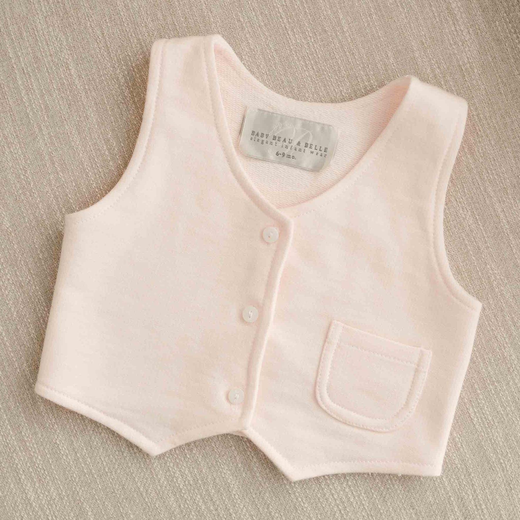A close-up of the Milo Blush Vest laid flat, showcasing the button front and small pocket.