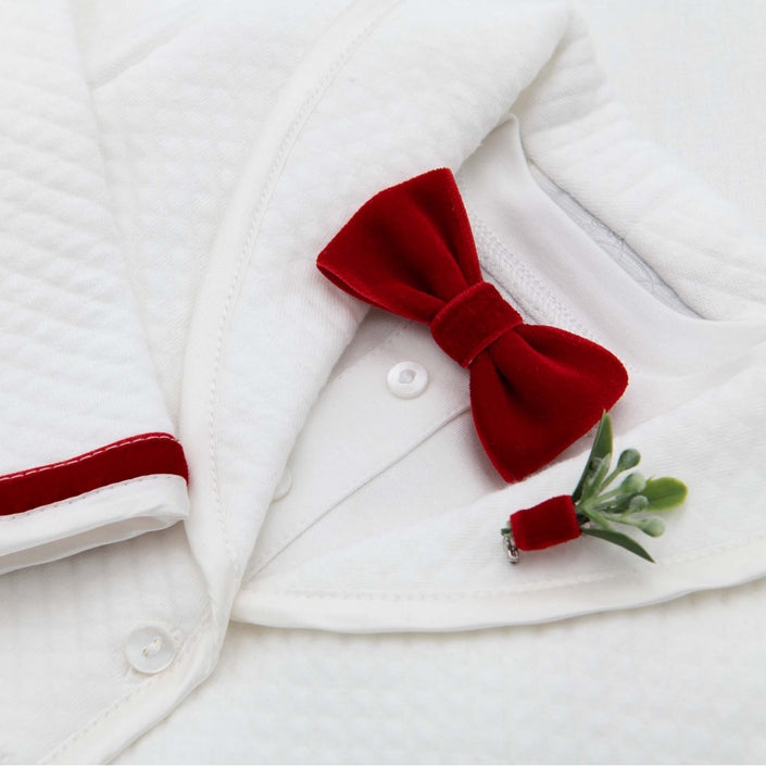 The Noah Red Bow Tie & Boutonniere features white textured fabric adorned with a handmade red velvet bow tie crafted in the USA, topped with a small green succulent boutonniere. The red velvet trim along the fabric edges makes it an ideal choice for holiday outfits.