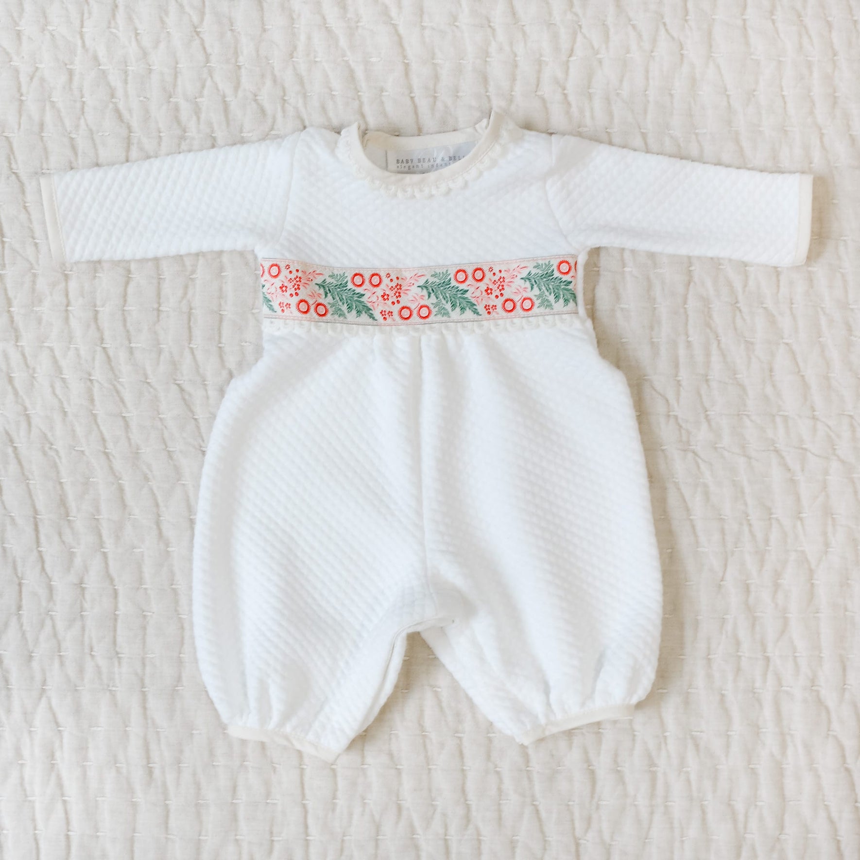 White baby romper with festive waistband on a textured beige surface