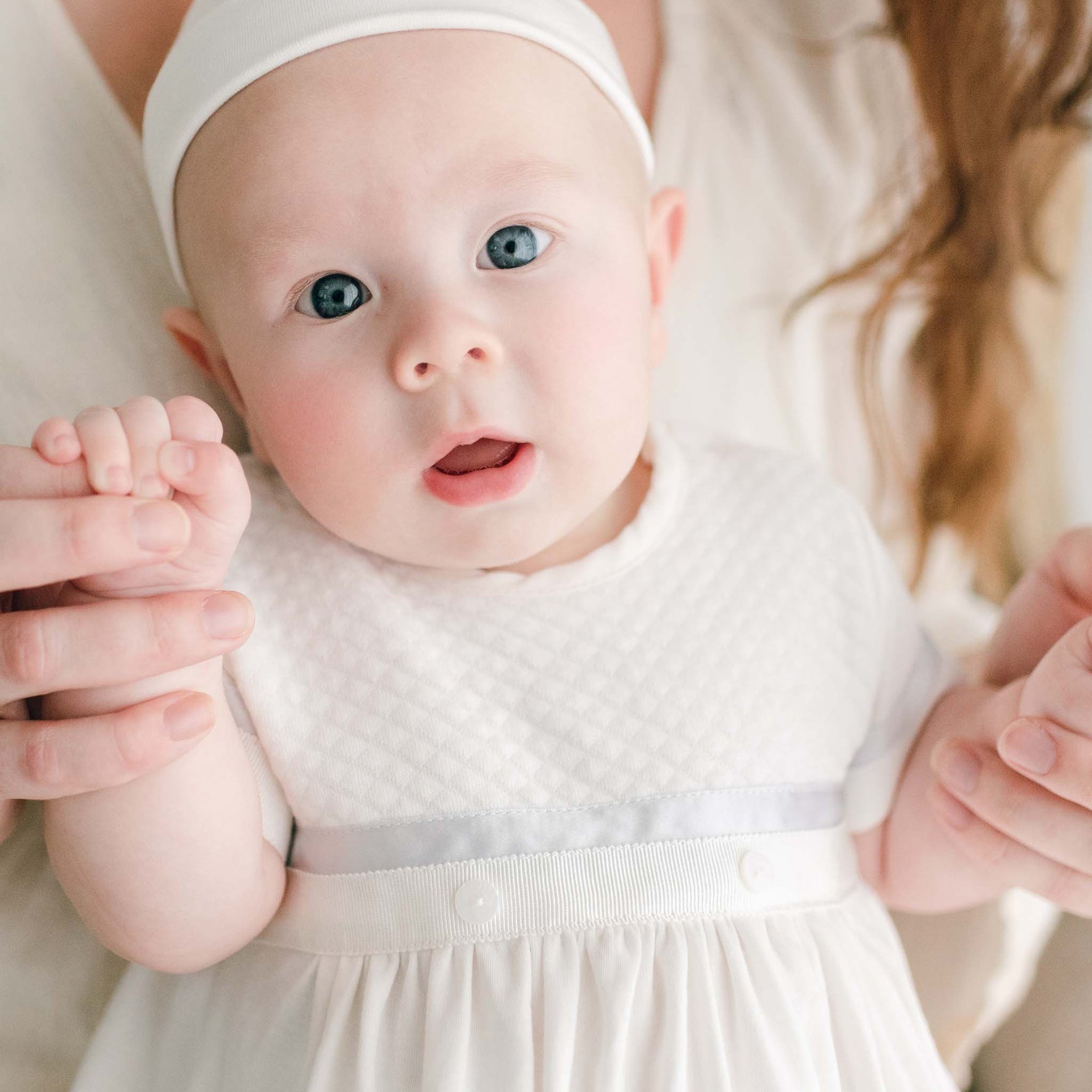 Close up photo of baby boy sitting on his mother's lap. He is wearing the Owen Layette and Knot Cap