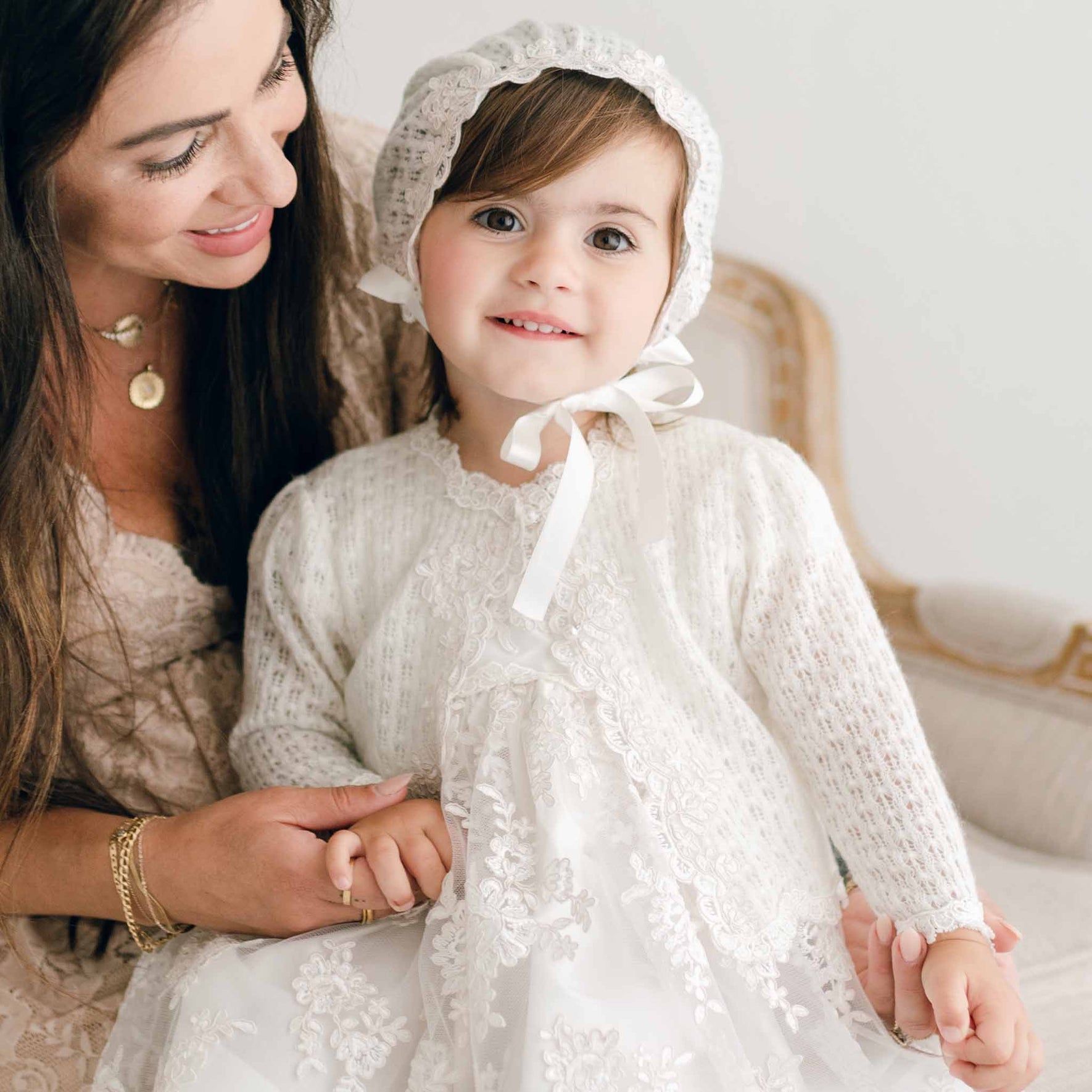 Baby girl wearing her Penelope knit sweater and bonnet. Pictured with her mom smiling.