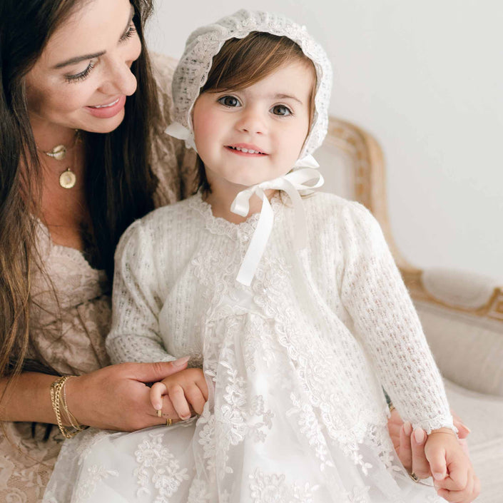Baby girl wearing her Penelope knit sweater and bonnet. Pictured with her mom smiling.