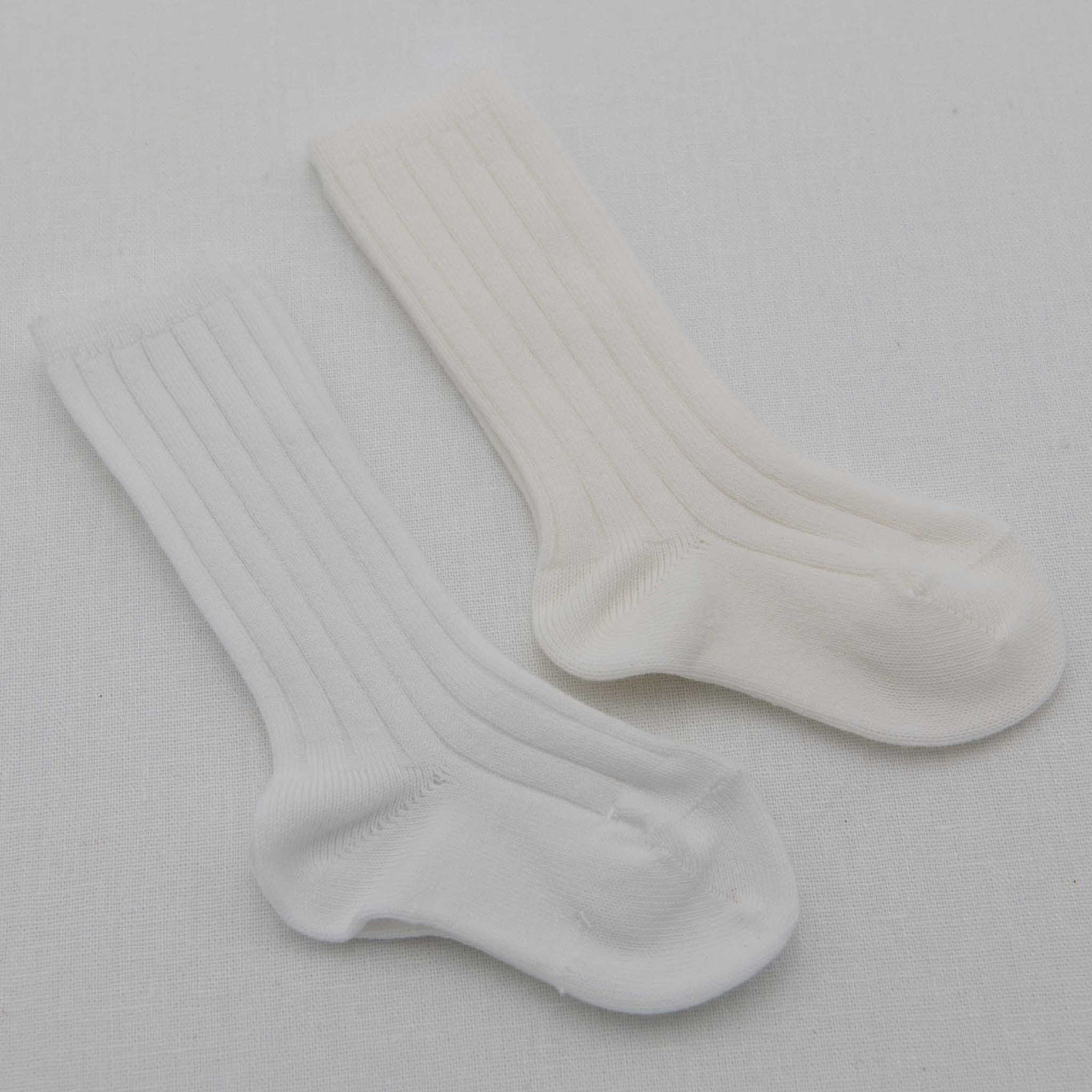 Flat lay photo of two pairs of socks, including both the white and cream Ribbed Knee Socks. These socks are made from a cotton blend and feature a ribbed pattern
