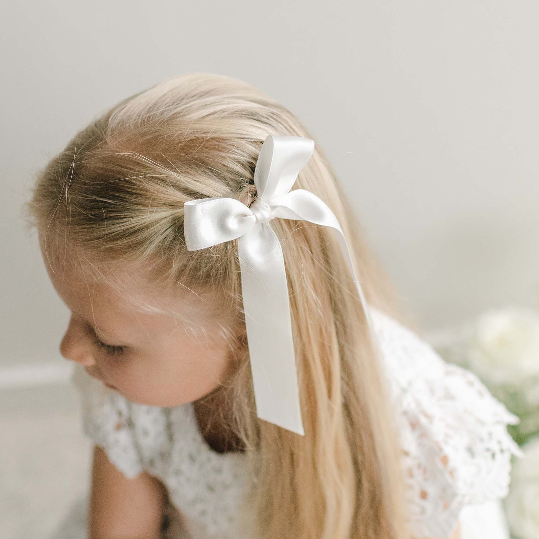 A close-up of a girl's hair adorned with a white silk ribbon bow, tied neatly with long trailing ends.