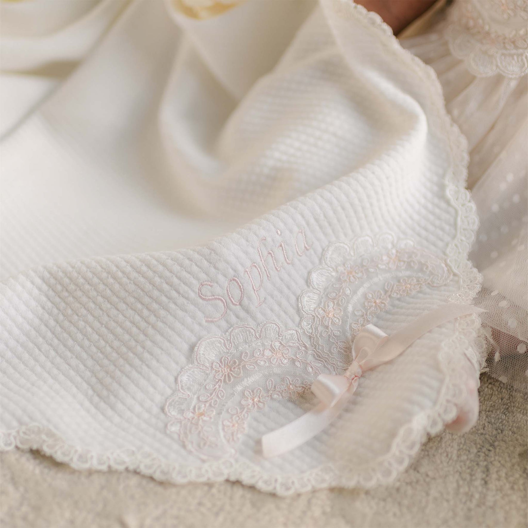 The Sophia Blanket embroidered with “Sophia” and lace detailing, folded over light lace.