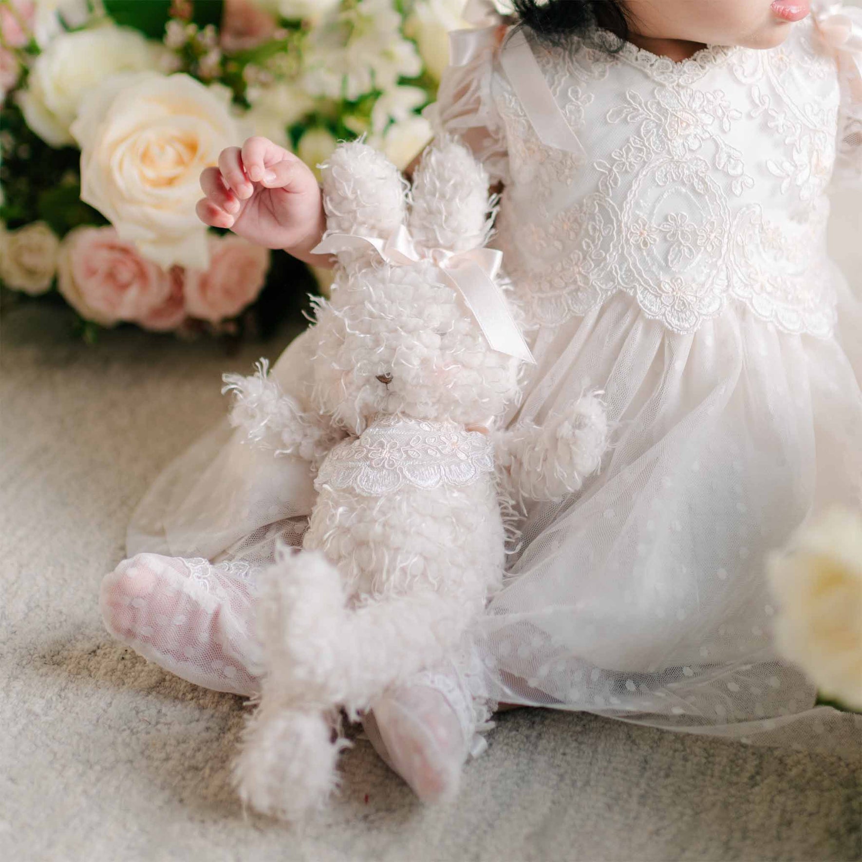 A plush Sophia Bunny with curly ivory fur and a lace-trimmed bodice, resting beside a baby dressed in a lace gown.