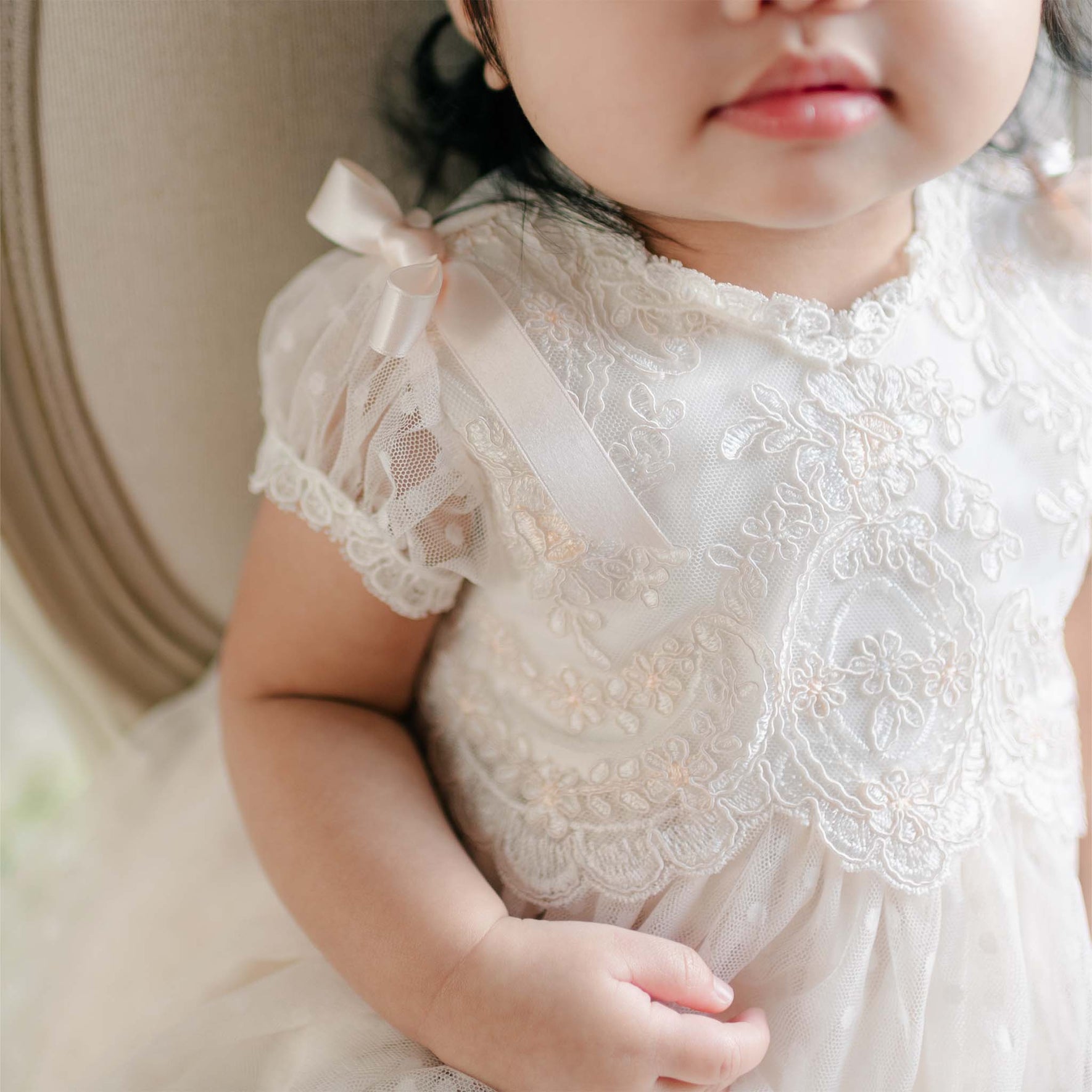 A close-up of the embroidered bodice of the Sophia Dress, highlighting the lace overlay and satin ribbon bows on the sleeves.