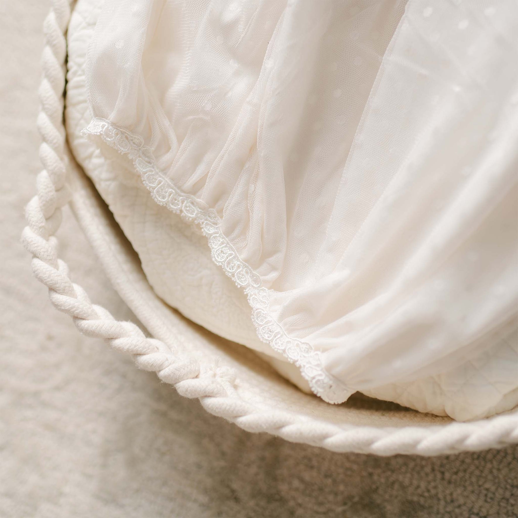 The bottom of the Sophia Layette's gown drapes over a bassinet, showcasing the delicate lace hem and soft gathered fabric.