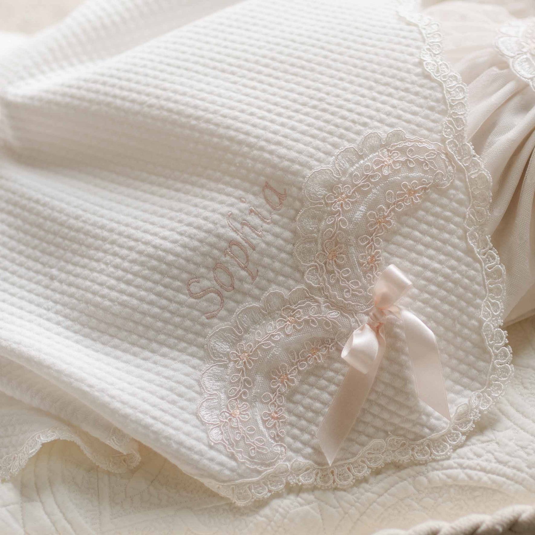 A detailed view of the Sophia Blanket showcasing the intricate lace embroidery, scalloped trim, and elegant satin bow accent, highlighting its heirloom-quality craftsmanship.
