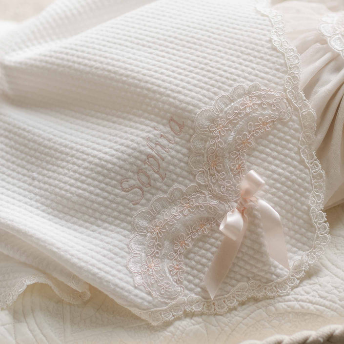 A detailed view of the Sophia Blanket showcasing the intricate lace embroidery, scalloped trim, and elegant satin bow accent, highlighting its heirloom-quality craftsmanship.