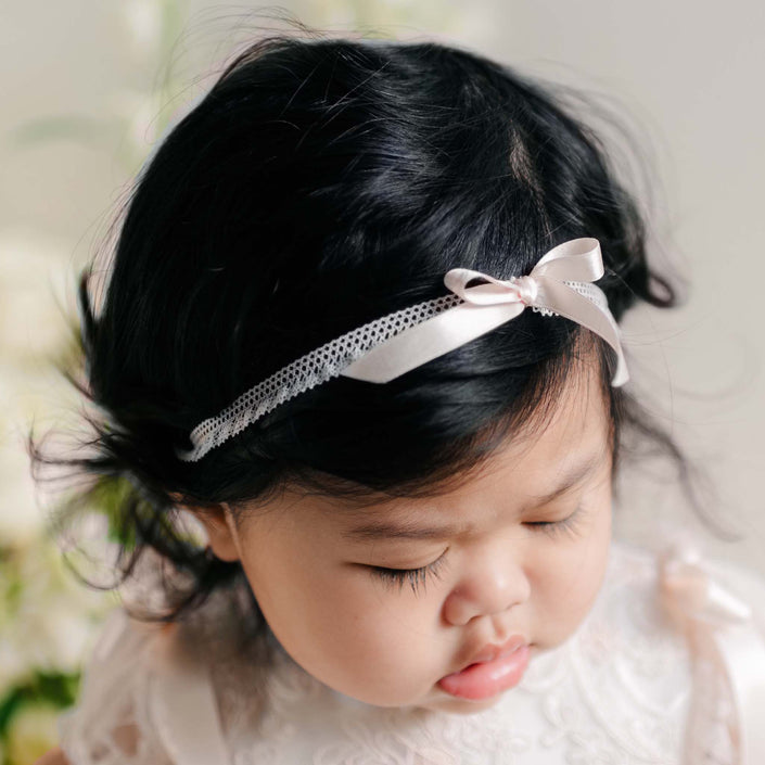 Close-up of the Sophia Silk Ribbon Headband on a baby's head, featuring a delicate satin bow and lace trim against dark hair.