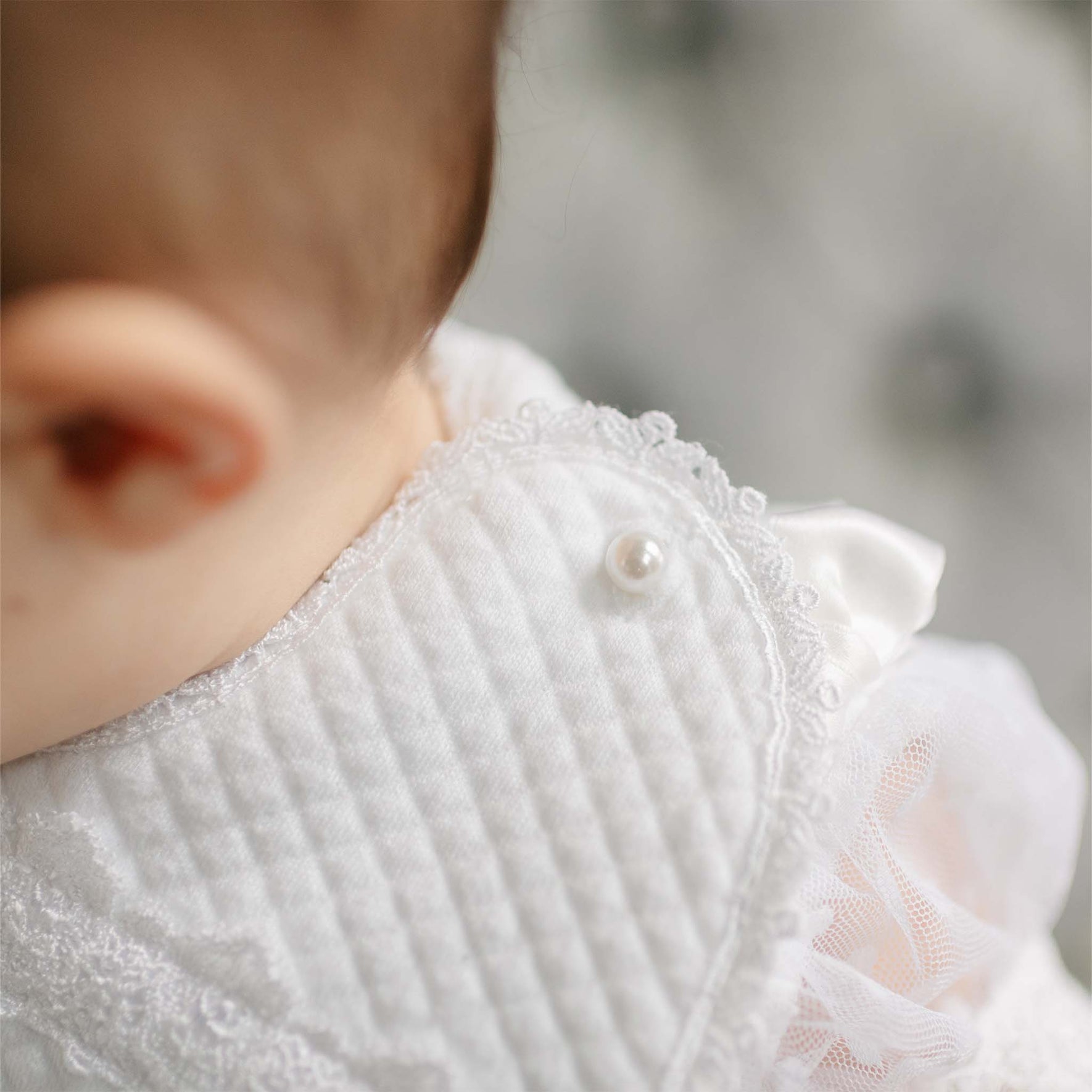 Close-up of the Stella Bib as worn on a baby against a blurred background. The details of the close up show a pearl style button closure on the bib.