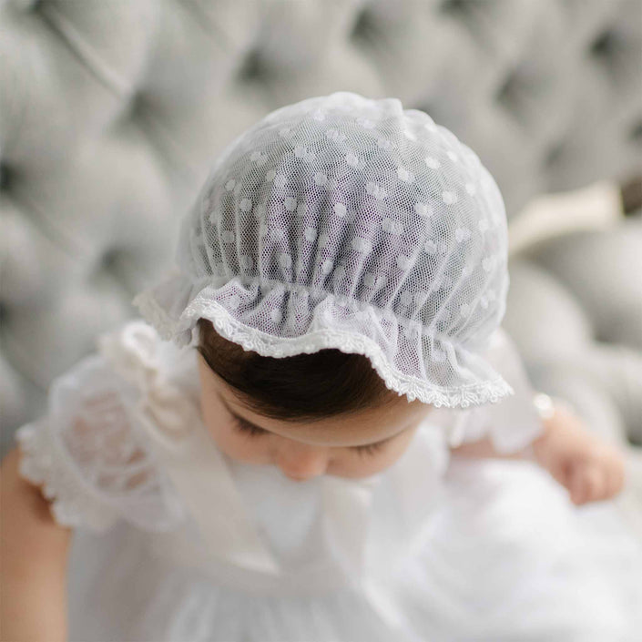 Top view of the Stella Lace Bonnet as worn by a baby. Details show the bonnet's white dotted lace and white edge lace trim in the front.