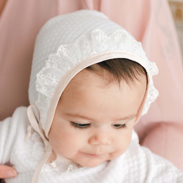 Newborn baby girl wearing the Tessa Quilt Christening Bonnet made from a quilted cotton in white and trimmed in pink champagne silk and light ivory floral lace.