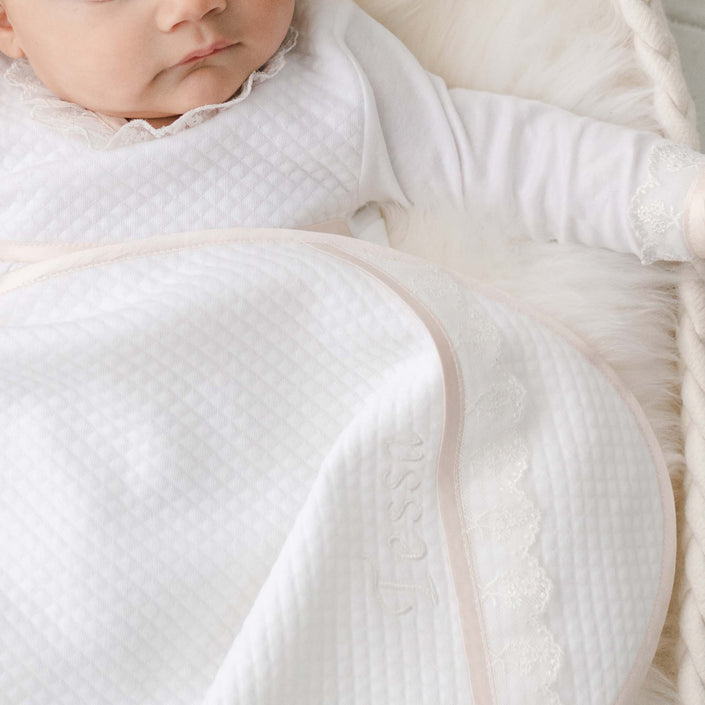 Newborn baby girl with the Tessa Personalized Blanket made from a textured cotton in white and featuring a ivory embroidered lace trim and personalized name embroidery. 
