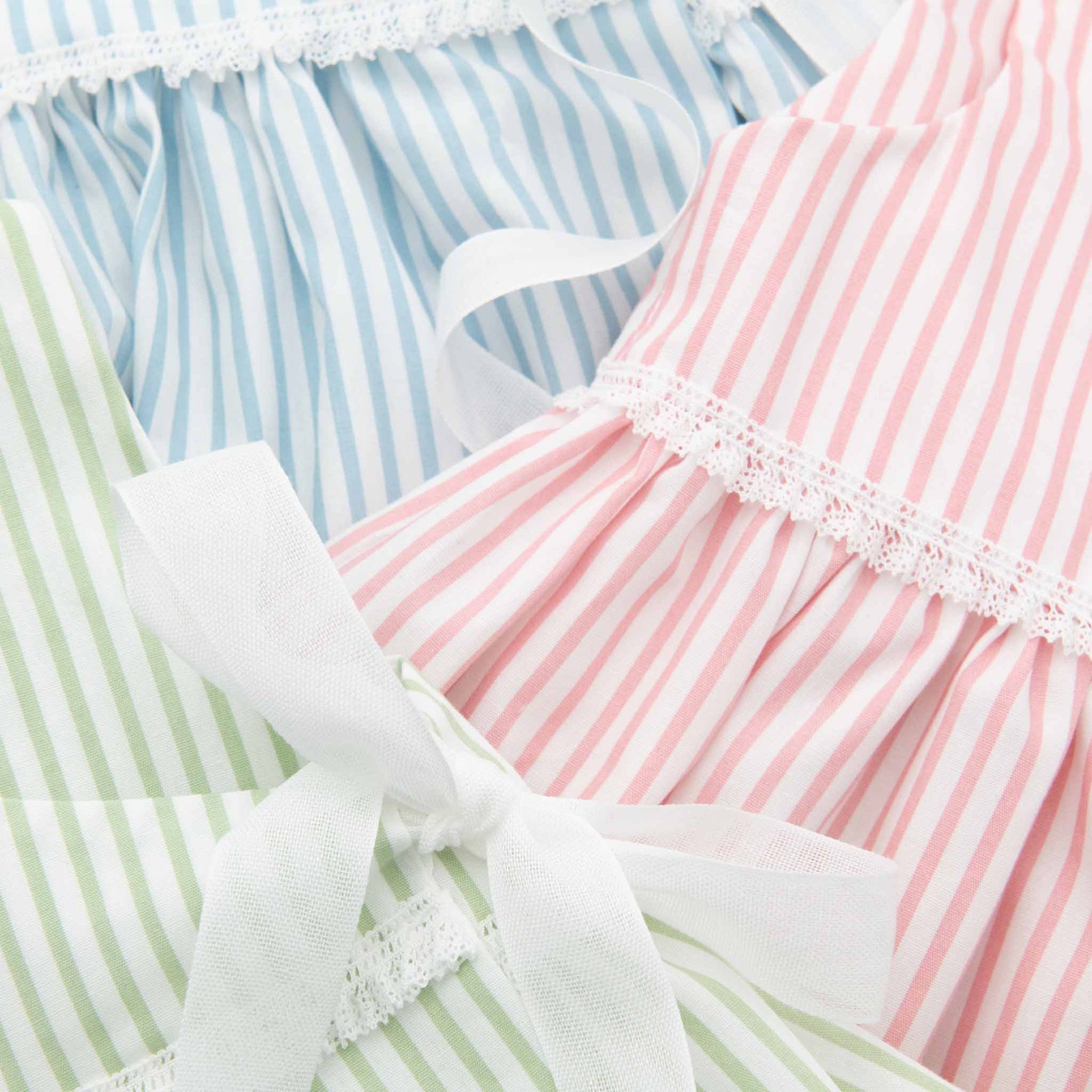 Close-up of Thea Wrap Dress in striped cotton, showcasing vertical stripes in blue, pink, and green. The material is accented with lace trim and a white ribbon tied in a bow, adding a soft, decorative touch.