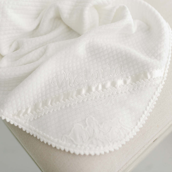 The Victoria Personalized Blanket, featuring a textured pattern in white, is elegantly draped over a light-colored surface. The name "Victoria" is beautifully embroidered in matching white thread near an ivory lace trim along the edge, making it an ideal personalized gift.