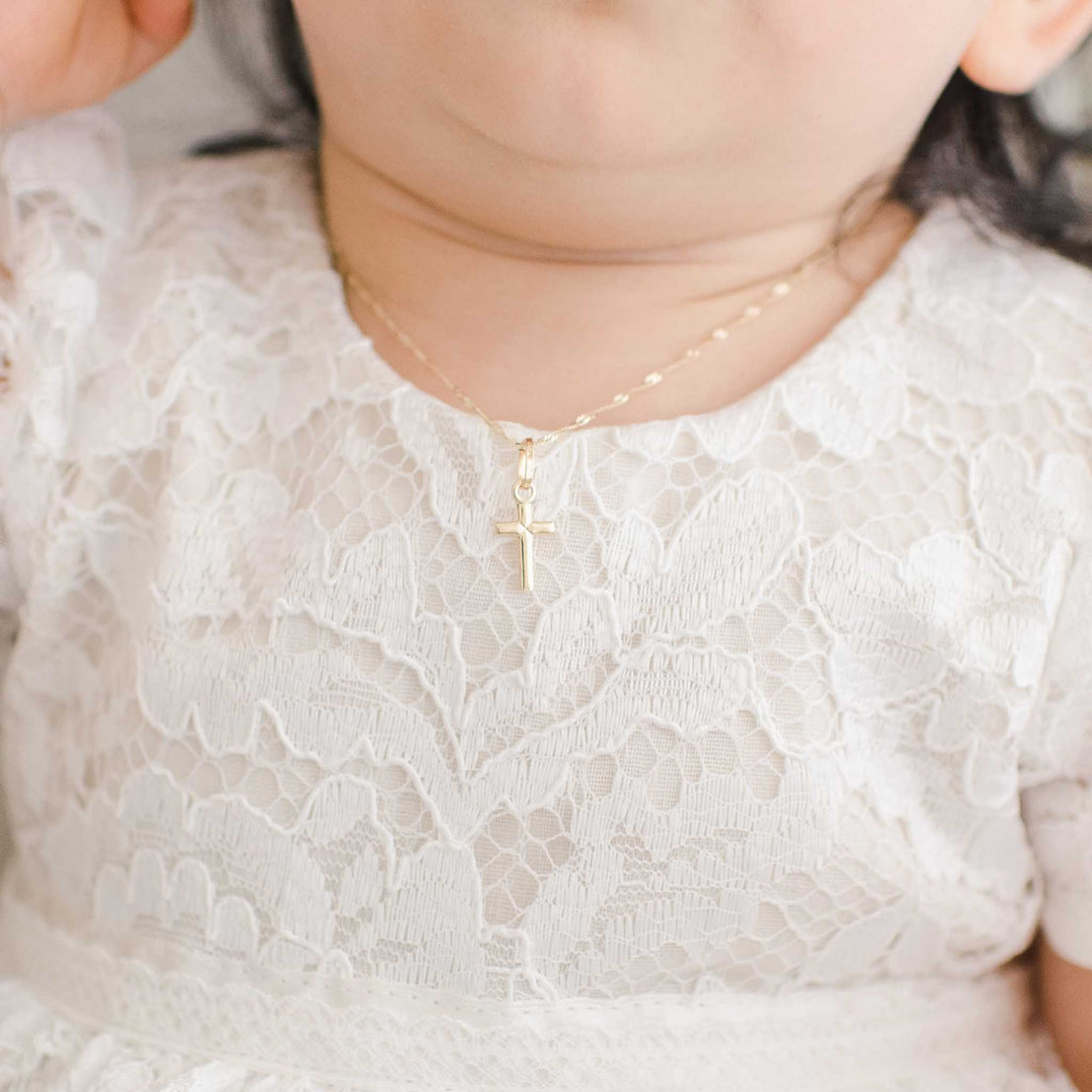 Small gold cross charm necklace on baby