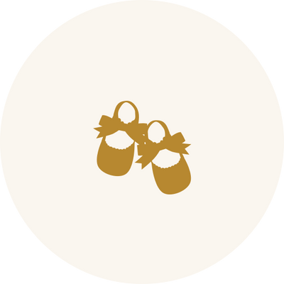 A pair of gold-colored baby shoes with bows on top, centered on a white circular background.