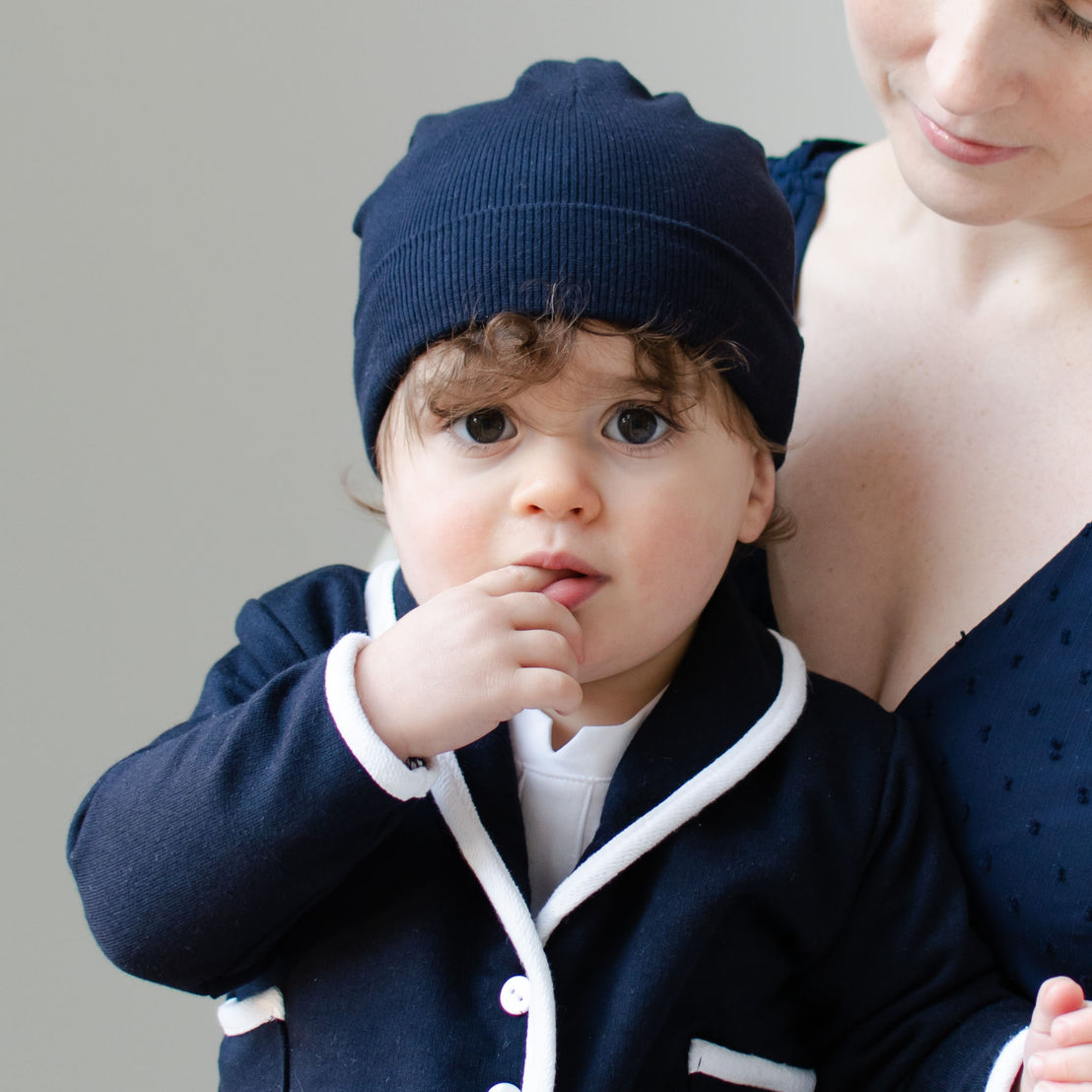 Closeup photo of a baby boy sitting with his mother and wearing the Navy Ribbed Pima Beanie and Elliott Jacket. 