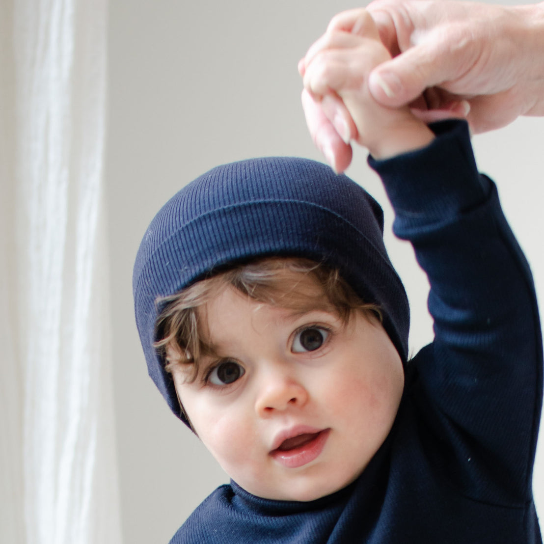 Photo of a baby boy wearing the navy Ribbed Pima Beanie made from 100% ribbed textured Pima cotton.
