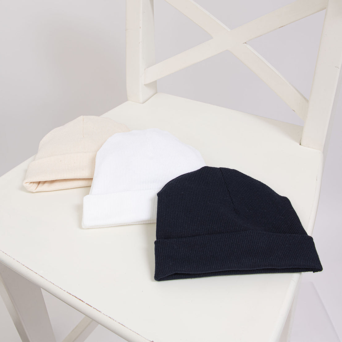 Flat lay photo of three Ribbed Pima Beanies in different colors, including ivory, white and navy.