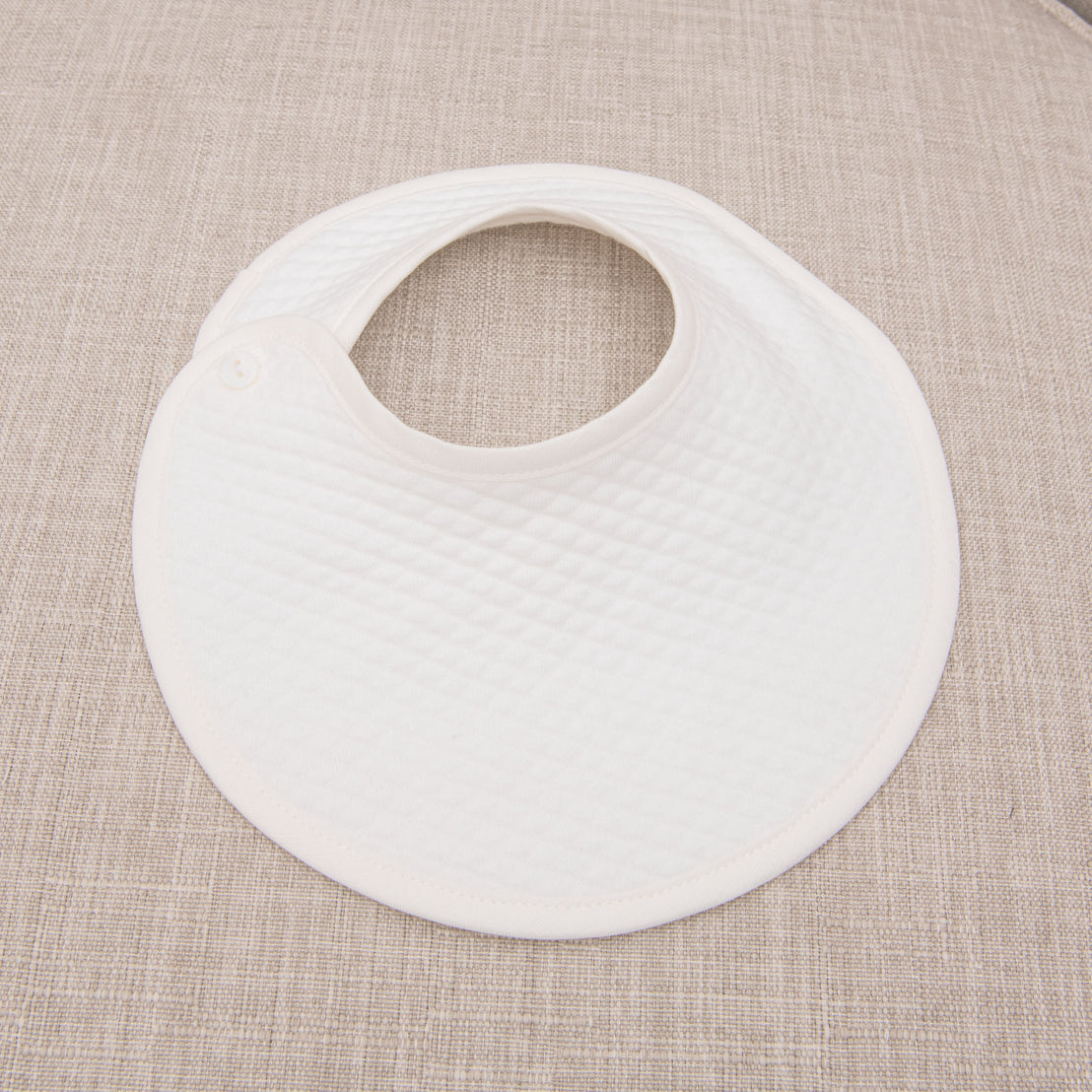 Boys baptism bib in white quilted cotton pictured on chair. 