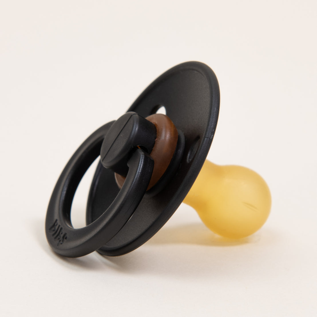 A Bibs Pacifier from Denmark, featuring a black round shield and a yellow nipple crafted from natural rubber, is set against a neutral background. This pacifier is designed to help babies self-soothe.