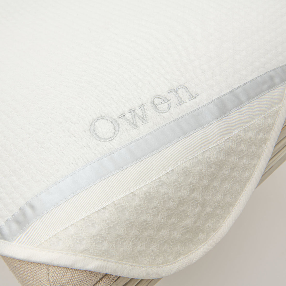 Closeup photo of the corner of the Owen Personalized Blanket. The corner features an ivory knit and the name "Owen" embroidered with light blue thread