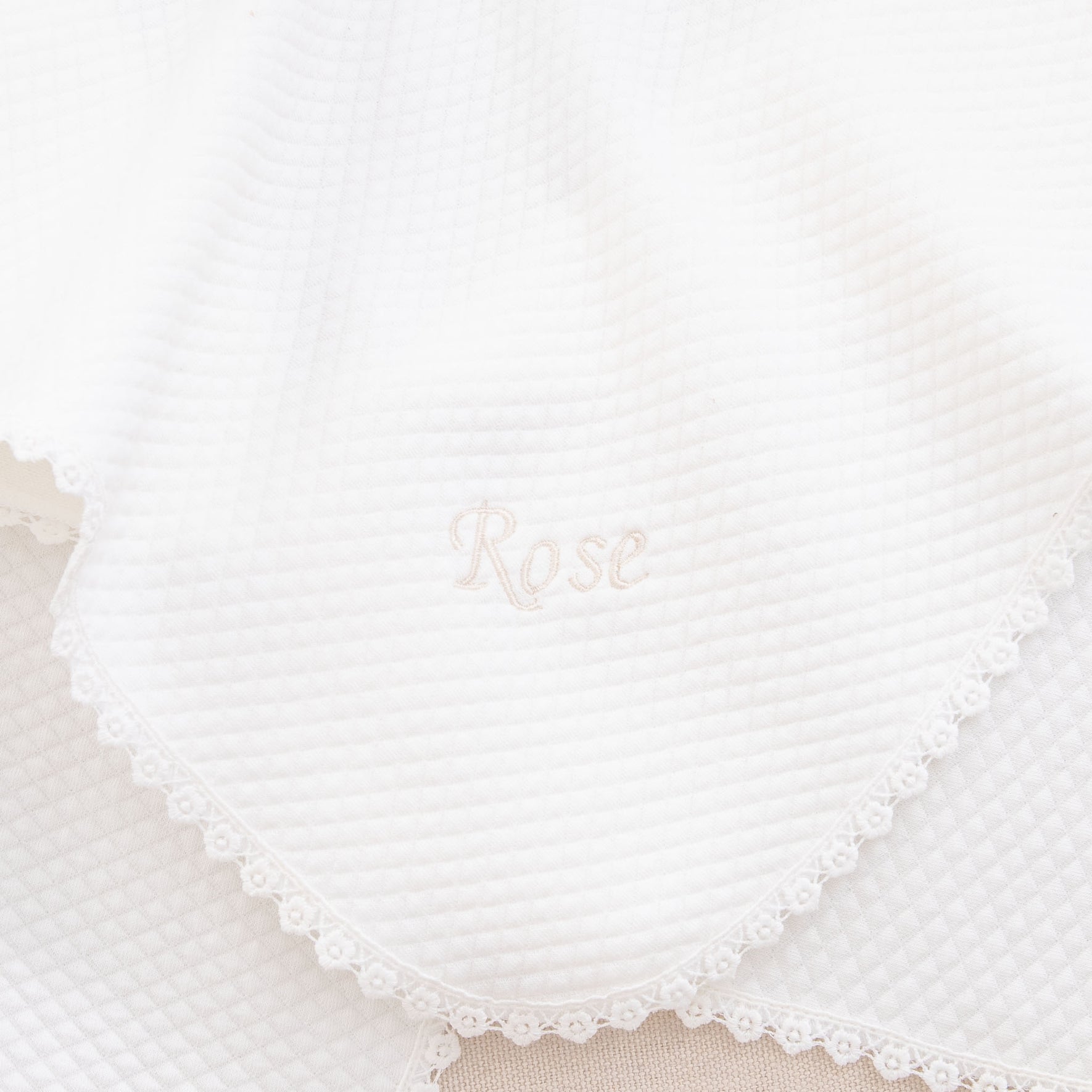 A close-up of a white textured blanket featuring lace edging, ideal as part of the "Rose Accessory Bundle - Save 15%" baptism set. The name "Rose" is beautifully embroidered in the center.