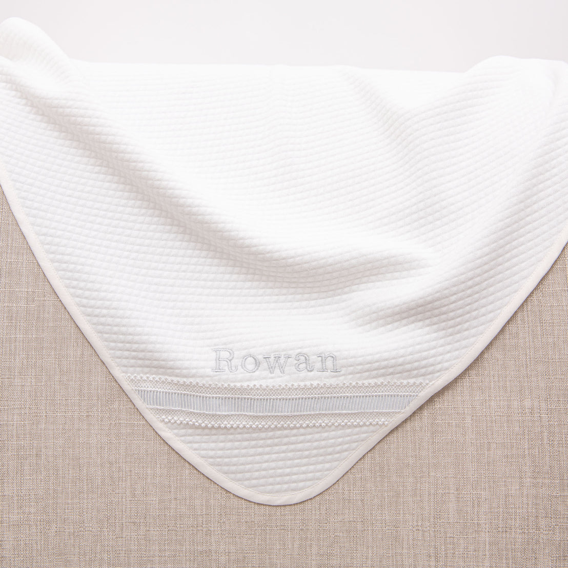 Hem detail on the personalized baptism blanket. Name 'Rowan' is embroidered in blue silk.