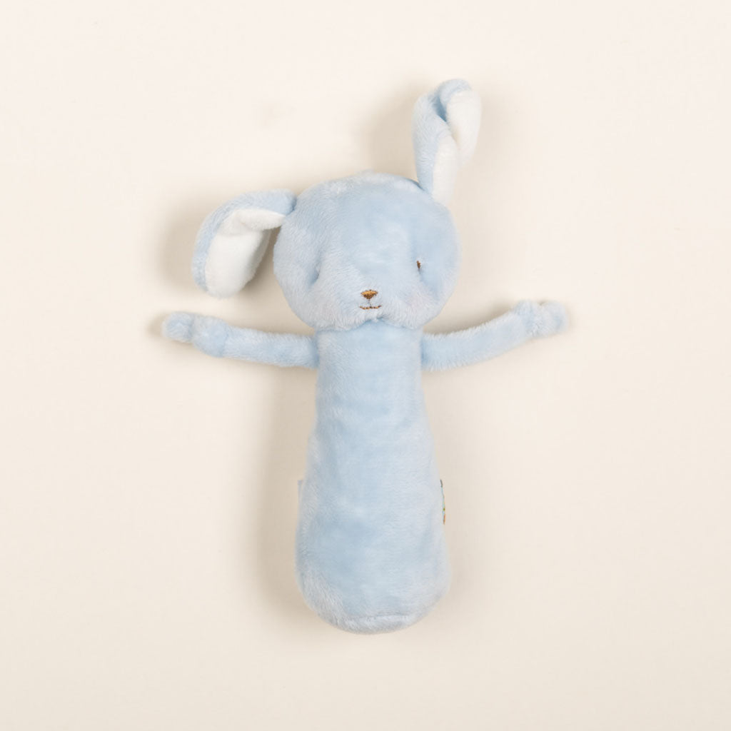 The Friendly Chime Rattle is a gentle, plush toy shaped like a bunny with long ears and small arms. It features soft embroidered details and is designed to be baby-safe. Styled on a plain, light background, this velour chime rattle comes in a soothing blue color.