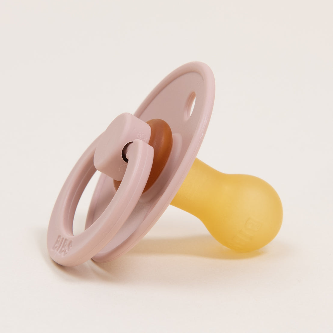 The Bibs Pacifier in Blush, part of a 2 pack set, is shown in a close-up shot featuring its pastel pink and yellow design crafted from natural rubber. This Danish-made pacifier, equipped with a circular handle, is ideal for aiding your baby in self-soothing as it rests on a plain white background.