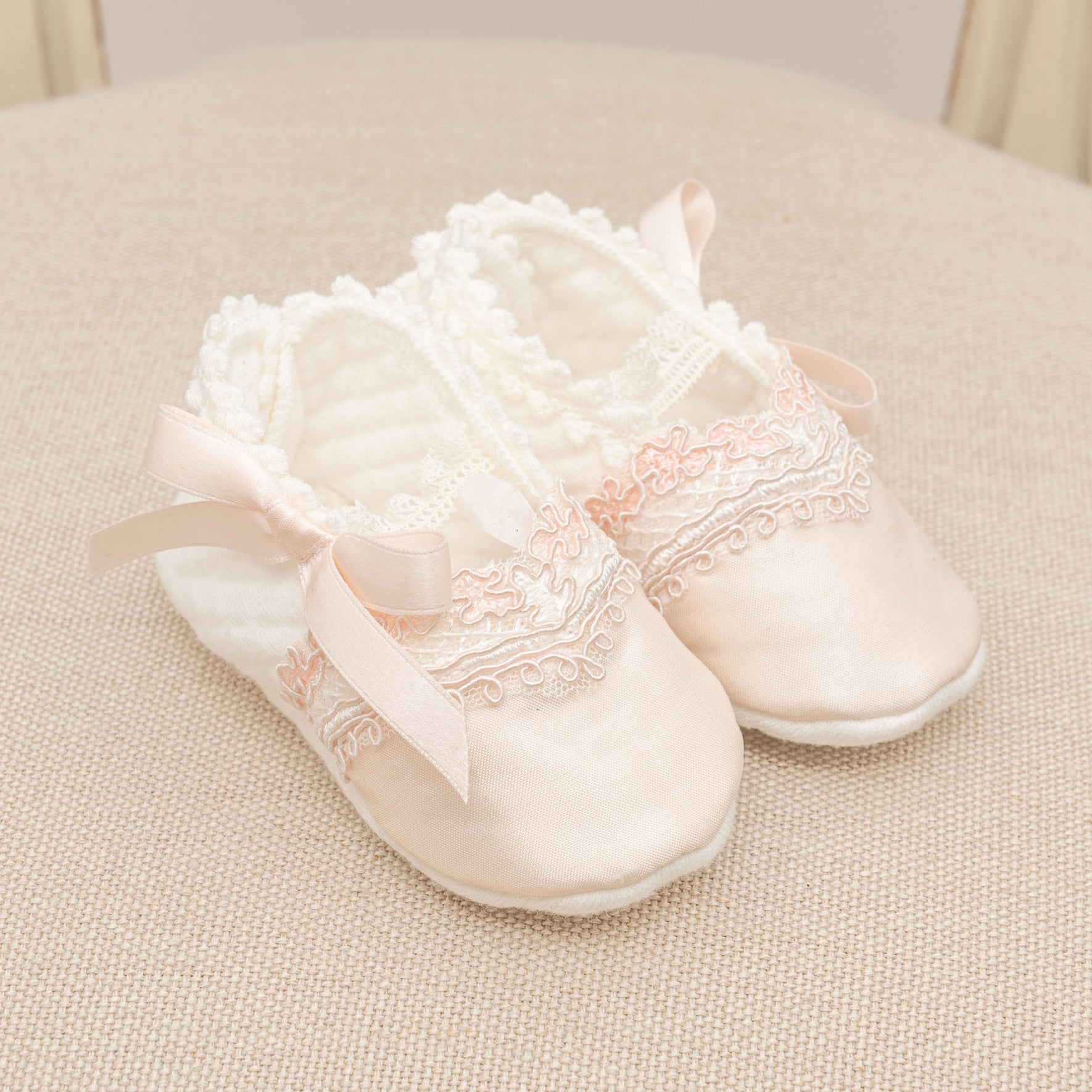 The Elizabeth Accessory Bundle - Save 15% features a pair of elegant pink baby shoes adorned with lace detailing and satin ribbons, ideal for enhancing a Christening outfit, displayed on a textured beige surface.
