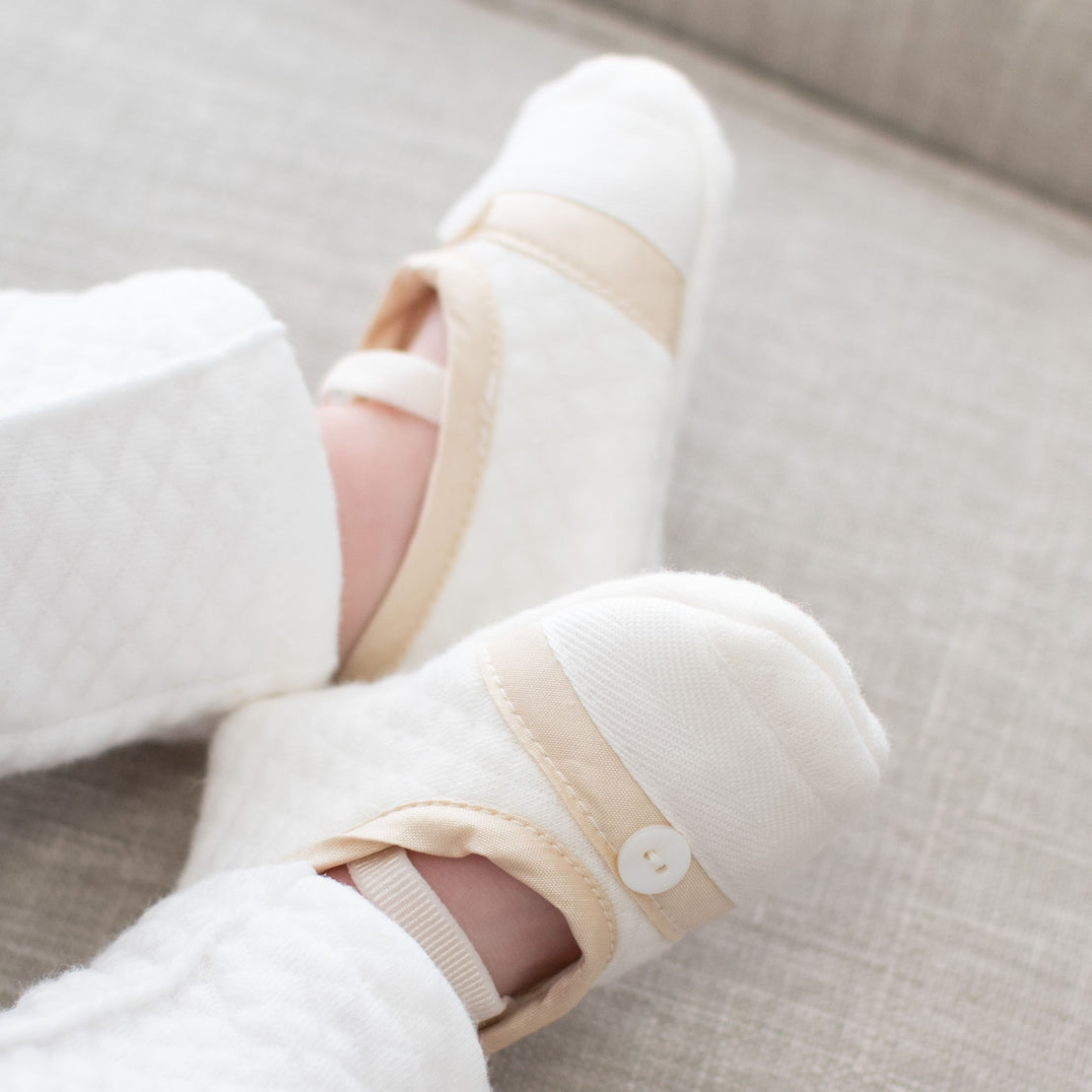 Boy wearing a pair of the Liam Booties made from soft quilted cotton with a champagne silk trim and accented with cotton ribbon and buttons on the toe. A soft elastic strap helps keep them on his feet