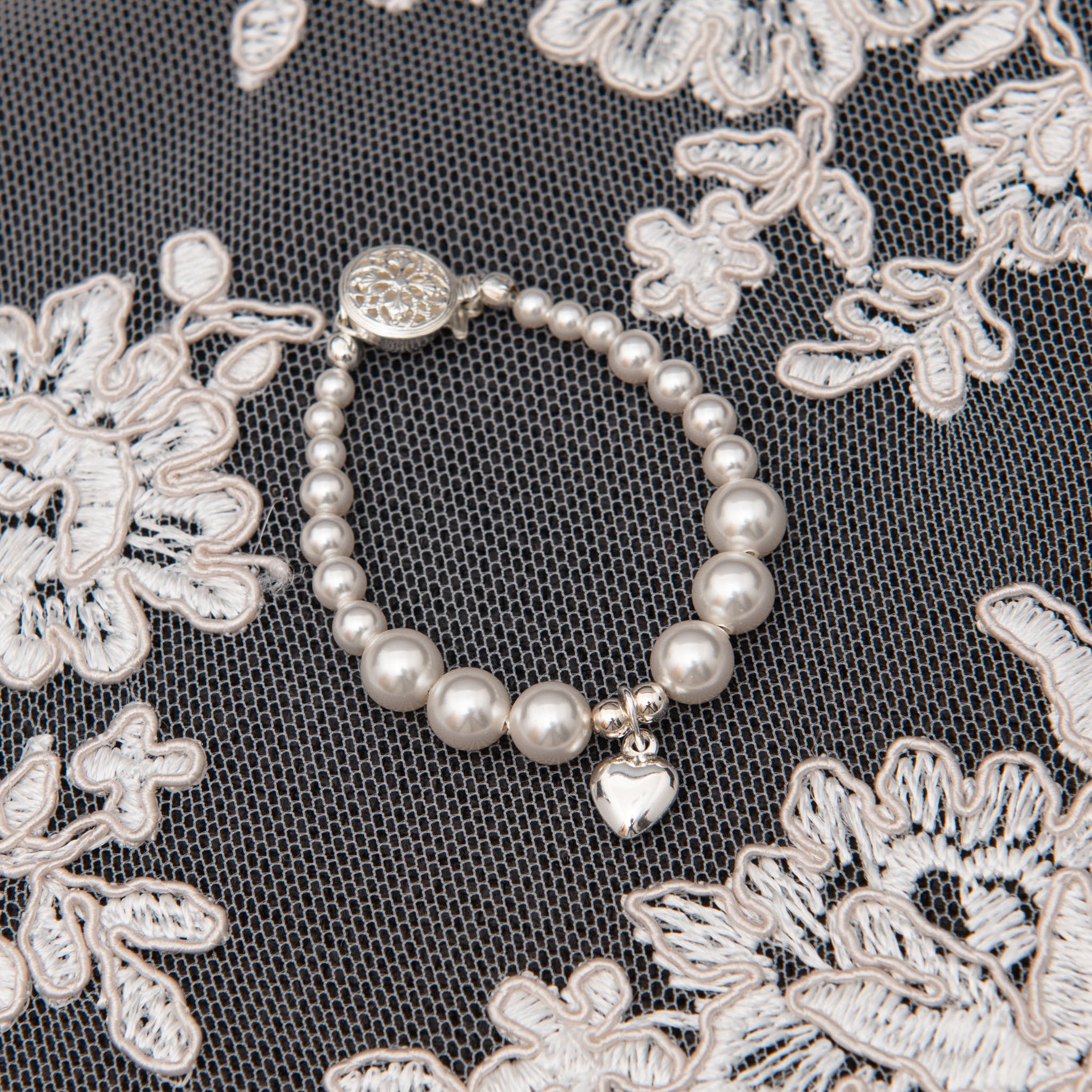Flat lay photo of the white luster pearl heart bracelet with silver heart charm. 