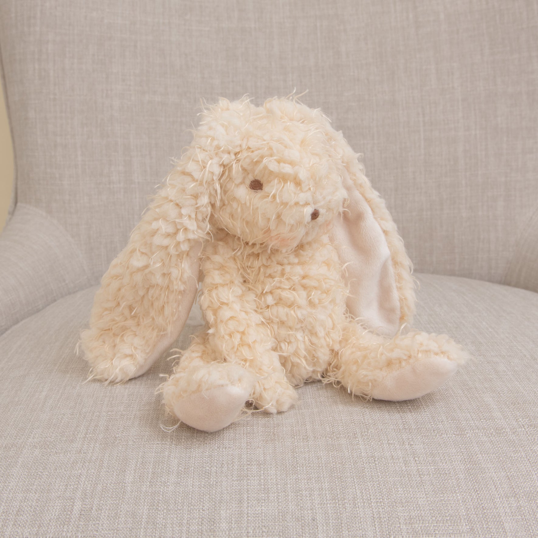 Photo of a super soft bunny stuffed animal made with warm almond scraggly fur body with embroidered face sitting on a chair