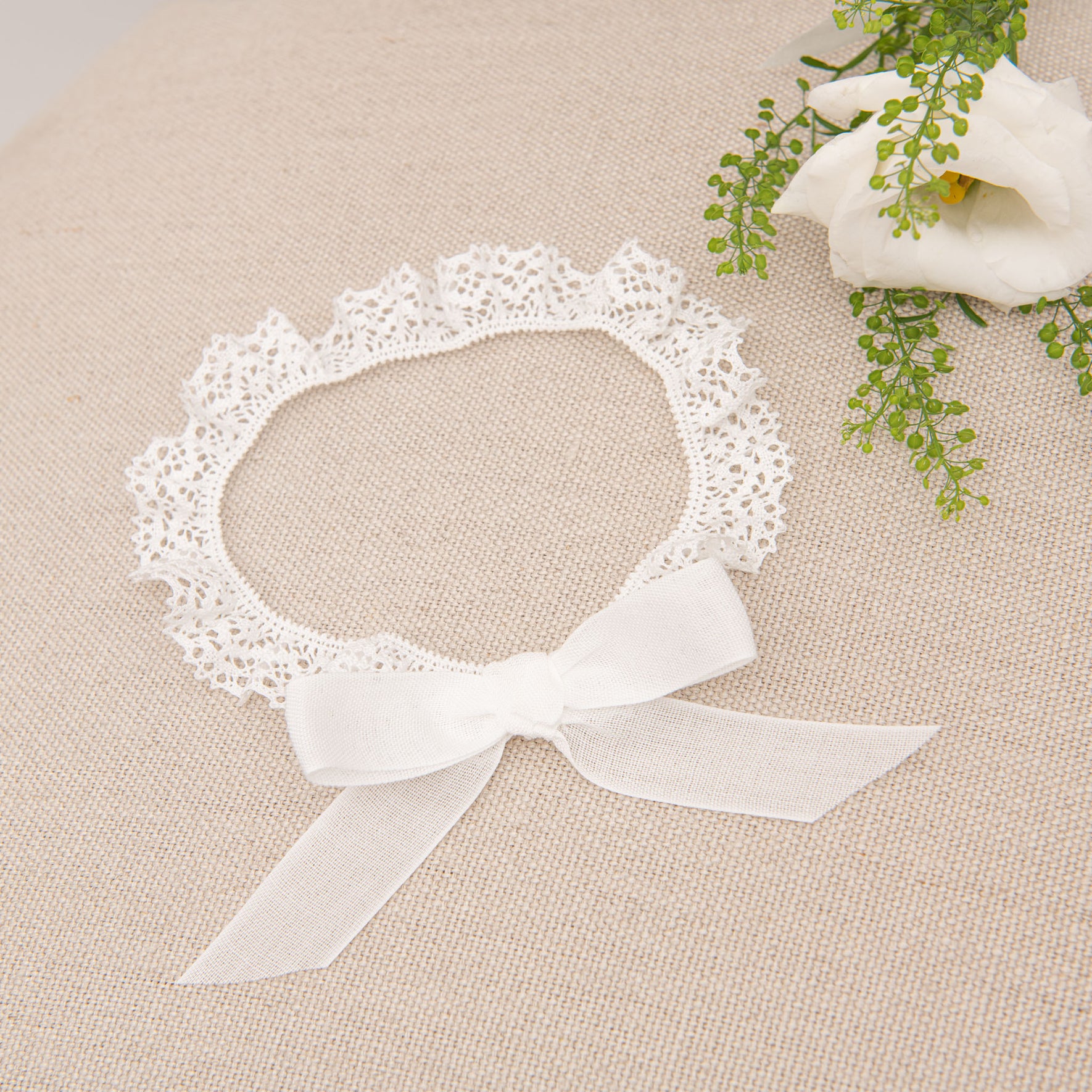 Detailed view of the Poppy Christening Headband, showcasing a white bow and lace accents, placed on a beige surface.