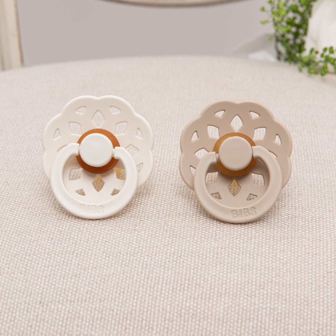 Two bibs pacifiers side by side in 2 colors: ivory and vanilla. 